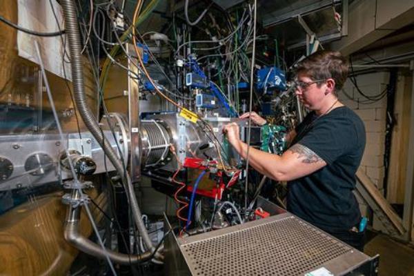 A scientist working on a piece of heavy duty machinery with stainless steel parts and lots of wires