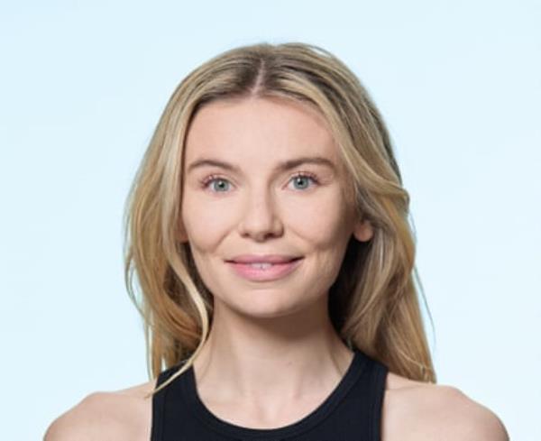 A portrait of Georgia Toffolo, with long blo<em></em>nde hair, and wearing a black vest top, shot against a pale blue background