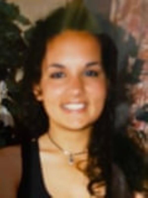 An old photograph of a smiling young woman with long dark hair, wearing a choker and a black, scoop-neck top