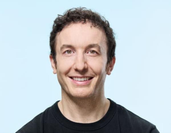 A portrait of a middle-aged man with brown hair, wearing a black T-shirt, shot against a pale blue background